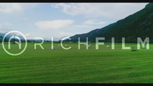 Aerial view of a field with finished hay bales and a view of the alpine region with overcast clouds