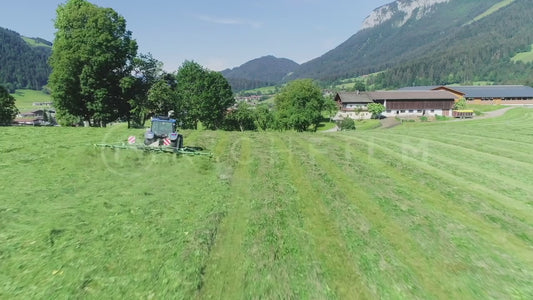 Aerial view of a tractor in the field turning hay with the Alps in the background