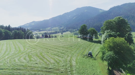 Agricultural aerial shots of a tractor in the field turning over its hay