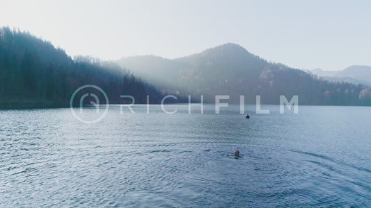 Aerial view of a lake with a swimmer and a wooded mountain landscape