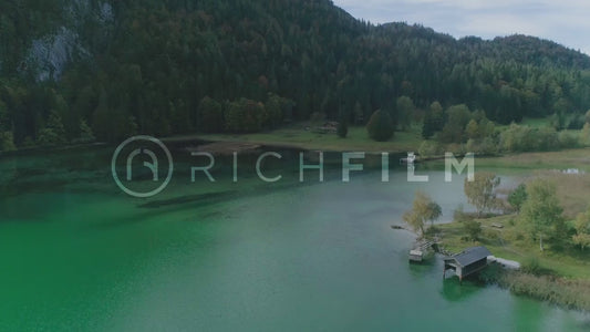 Aerial view of a green lake with mountain and forest and a lake hut