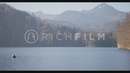 shot of a lake with orange wooded mountains and bright sunshine