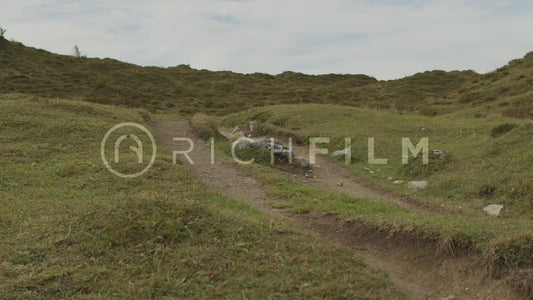 Slow motion shot of mountain biker riding up a green hill, front view in summer - V2