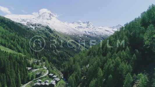 Aerial view of slightly white mountains and green forest with small hats