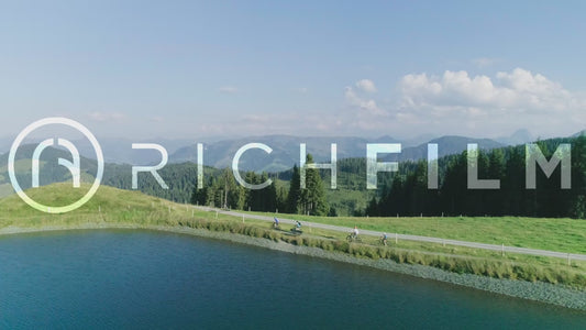 Aerial view of cyclists cycling around a lake with a view of a hilly landscape - V2