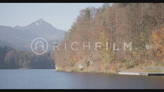 Shot of a lake, clear sky with mountains and orange-coloured forest