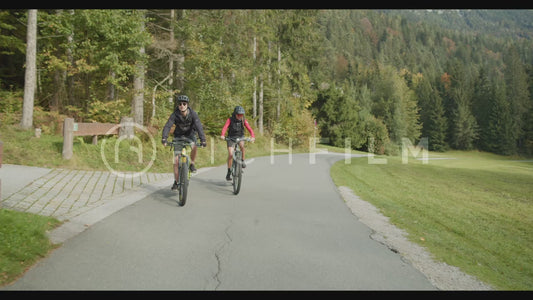 shot of mountain bikers riding on a road next to a lake with mountains in the background - V2