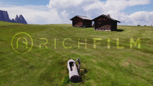 Aerial view of wooden huts on a hilly landscape with the Dolomites as a backdrop