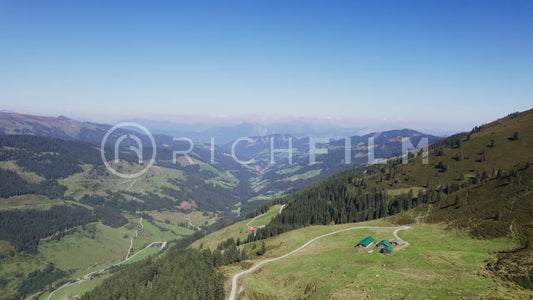 Drone shot of mountain landscape with forest and huts under a blue sky