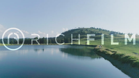 Aerial view of cyclists cycling around a lake with a view of a mountain railway and a forest - V2