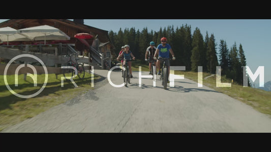 Shot of mountain bikers riding on a road in the Alps with forest and clear sky