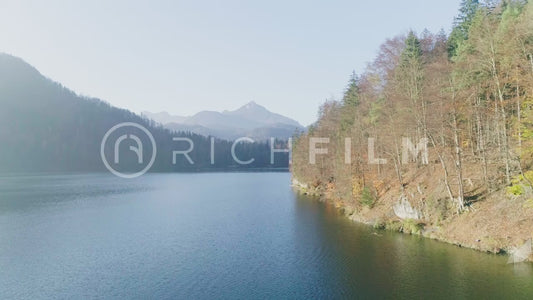 Shot of a lake with rays of light in the blue water and clear sky with mountains and orange forest - V2