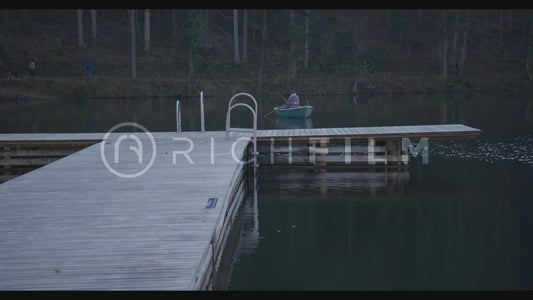 Shot of a drifting rowing boat on the lake, forest and a wooden jetty