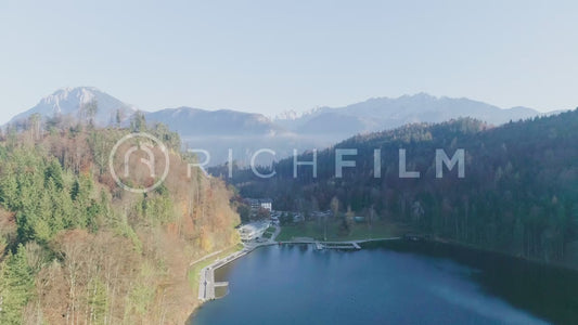 Aerial view of the blue lake towards a shore with mountains, clear sky and autumn forest