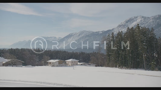 Shot of a snow-covered field with forest and view of the mountains