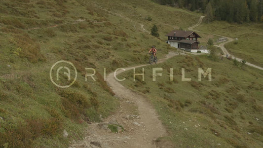 Slow motion shot of a mountain biker riding up a hill with a house in the background