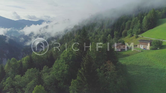 Aerial view of a mountain landscape with house, forest and low clouds