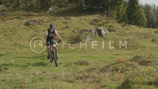 Slow motion shot of two mountain bikers riding up a green hill, front view in summer