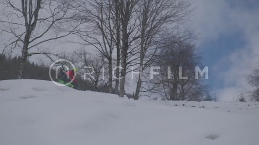 Slow motion shot of a mountain biker riding down a snow covered hill, from the side view